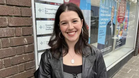 BBC A young woman with dark hair smiles at the camera. It is a head and shoulders shot.