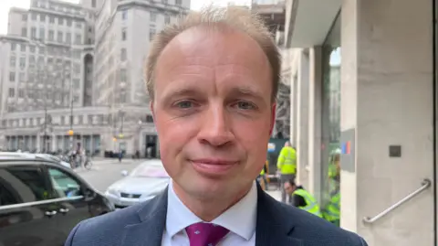 A close-up head shot of Southampton Itchen MP Dr Darren Paffey. He is wearing a suit and tie and is smiling slightly as he looks into the camera.