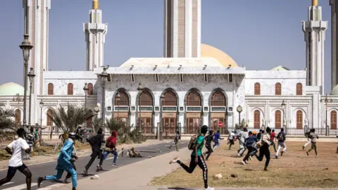 AFP Protesters run past a mosque during clashes with police in Dakar, Senegal - 9 February 2024