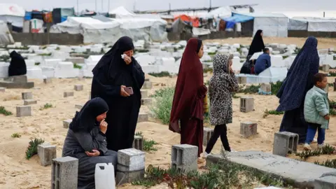 Reuters Palestinian women visit graves of relatives killed during the war in Gaza, at a cemetery in Rafah (10 April 2024)