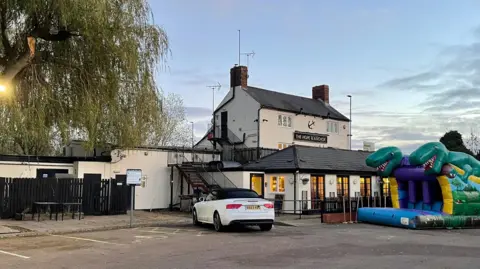 A white pub building with an anchor logo on its frontage and a partially deflated bouncy castle out front