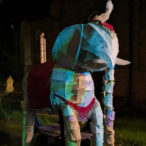 Historic Coventry Trust A wire frame model of an elephant, covered in multi-coloured fabrics and topped by an Indian-style head covering and a feather sticking out.