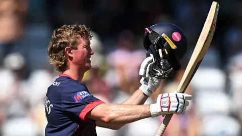 Keaton Jennings smiles as he raises his bat and helmet to celebrate his century for Lancashire against Somerset at Taunton on Tuesday, 11 August, 2026
