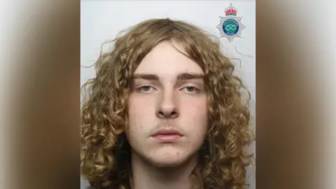 A mugshot of a boy with long curly blonde hair.