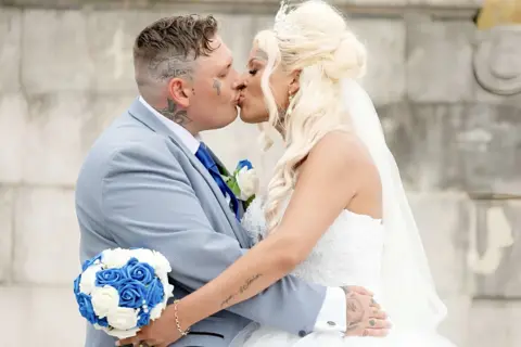 Supplied A man in a light blue suit and a woman in a white wedding dress sharing a kiss.