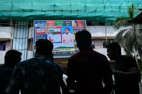 AFP عابران پیاده قیمت سهام را به صورت دیجیتالی در خارج از بورس اوراق بهادار بمبئی (BSE) در روز اعلام نتایج انتخابات عمومی هند در بمبئی، 4 ژوئن 2024 تماشا می کنند.