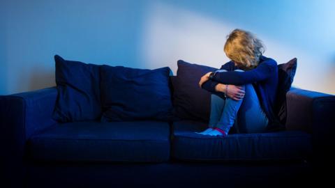 A woman showing signs of depression sat on sofa