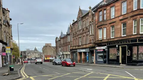 BBC Cars travelling past three-story residential and commercial properties as they go along Quarry Street