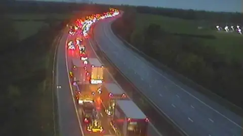 A three lane motorway with one carriageway full of cars and the other empty