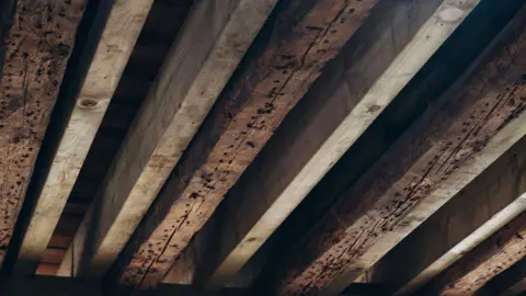 Caister and District Community Trust A series of nine, brown wooden roof beams, with dark tool marks showing in the wood
