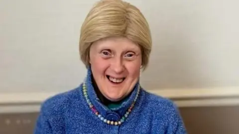 Woman with short blonde hair smiling at camera in blue wool cardigan and beaded necklace 