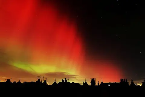 Susan Duncan The orange and green glow of the Northern Lights over silhouetted rooftops.