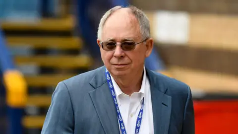 New Reading owner Rob Couhig pictured wearing sunglasses, a suit and an EFL lanyard around his neck. He is balding with grey hair