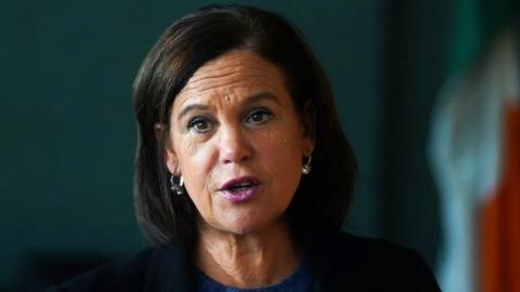 Mary Lou McDonald in dark suit jacket against green backdrop