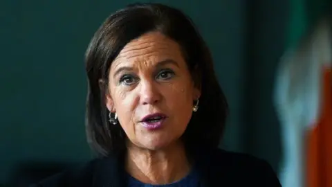 PA Media Mary Lou McDonald in dark suit jacket against green backdrop