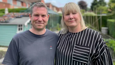 Brother and sister Richard Bettany and Victoria Shipley are pictured together looking at the camera. Victoria is wearing a black and white-striped shirt and has shoulder-length black hair. Richard, to the left of the image, has short grey hair and is wearing a grey shirt.