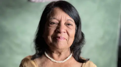 Indu Sharma smiling at the camera wearing a white necklace and light brown saree