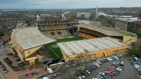 BBC Aerial picture of Wolverhampton's Molineux stadium, showing the stands, cars parked in front and city buildings behind