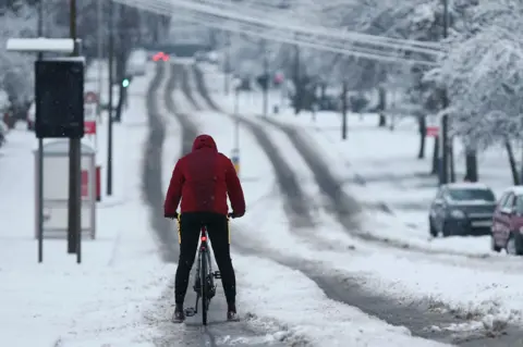 Getty Images A cyclist rides down a snow covered road as heavy snow falls down on the West Midlands overnight on 28 December 2020 in Stourbridge, England