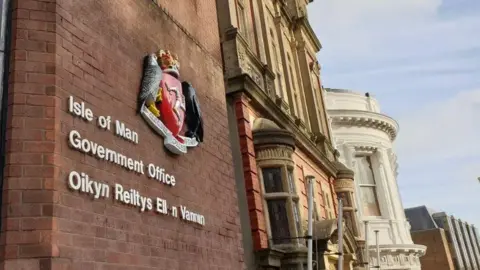BBC The outside of a red brick building with a government crest and lettering on the wall