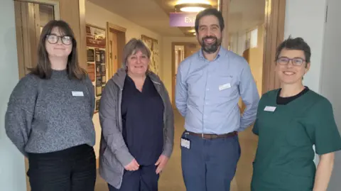 ReMind UK The photo shows the research team at ReMind UK.  The three women and a man are standing in a corridor and are smiling into the camera.