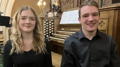 Ellen Taylor and Kyle Bradshaw sit in front of an organ