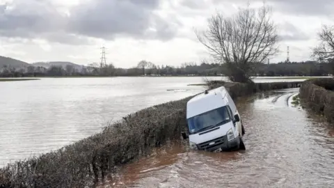 PA Media A van sits in floodwater near the village of Hampton Bishop near Hereford, after the River Lugg burst its banks in the aftermath of Storm Dennis