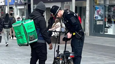 Leicestershire Police A police officer inspecting an Uber Eats delivery driver's e-bike on a pedestrianised city centre street