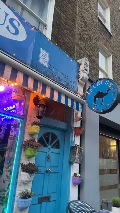 Blue front door of restaurant with camel sign below the word 'Acacus'