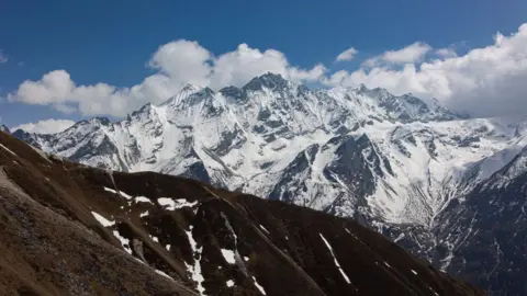 Getty Images Snow-covered mountains in the Himalayas, in front of a thin band of cloud on a blue sky