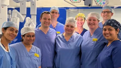 Nine people in blue scrubs standing and smiling in an operating room.