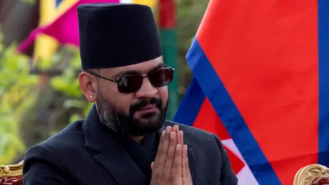 EPA Balendra Shah wears a traditional Nepalese black hat and sunglasses and a dark suit, and has his hands clasped in prayer in front of his face