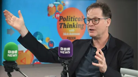 BBC Nick Clegg gestures with his hands as he speaks in the Political Thinking studio. He wears a dark suit and a dark grey, open-necked shirt.