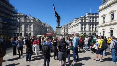 PA Media Crowd gathers around a statue in central London, with historic buildings lining the street