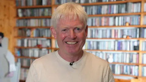 Kevin in front of his vast CD collection arranged on shelves.