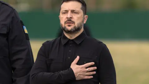 Volodymyr Zelensky dressed in all black with his right hand placed across his chest.