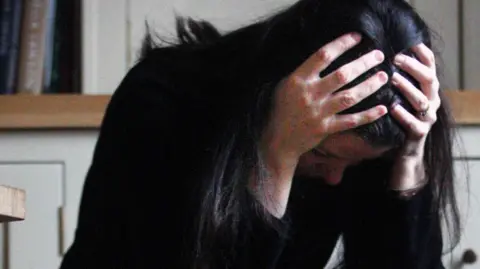 Image posed by a model of a woman holding her head in her hands.