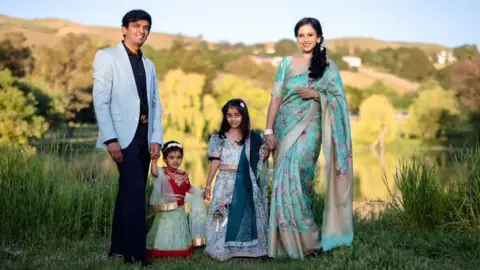Nithin Hassan Nithin Hassan wearing a powder blue blazer (L) with his two daughters in the centre and his wife on the right wearing a traditional Indian saree, pose for a photograph. 