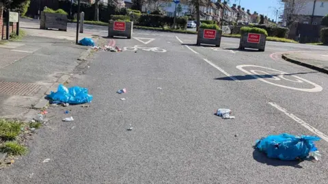 Rubbish bags can be seen across a road, with rubbish spilling out of them