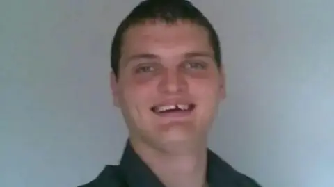 Family handout Kyle Marshall has blue eyes and short cropped dark hair. He is wearing a black shirt and is smiling at the camera. Behind him is a plain grey background.