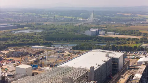 Industrial estate with the paper mill in the foreground with the landscape of Deeside behind (there is greenery and a bridge in the back of the image.)