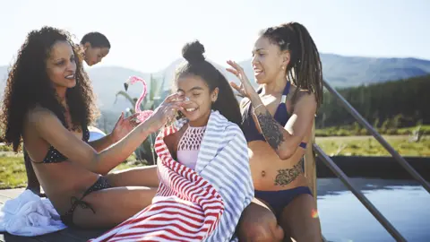 Getty Images Family applying sunscreen by pool