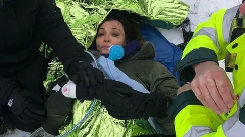 sarahparish23/Instagram Actress Sarah Parish laying on the snow under a foil blanket and being treated by paramedics