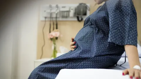 Getty Images Pregnant woman in a gown sitting on a hospital bed