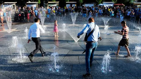 Getty Images President Volodymyr Zelensky (L) and children refresh themselves in a fountain during his first official visit to Mariupol on 15 June 2019