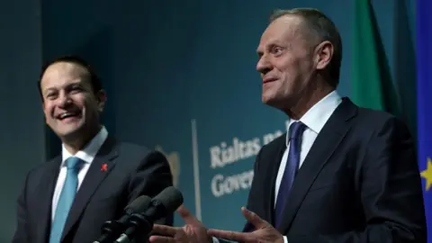 PA Leo Varadkar laughs as Donald Tusk, smiling, addresses the media from a podium