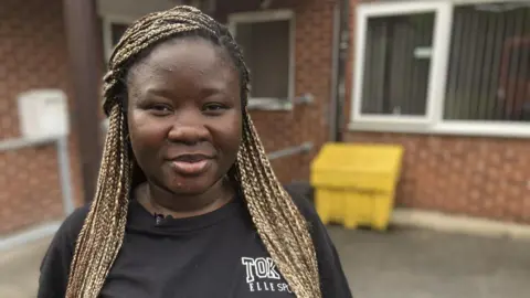 Yemi a care worker stood outside the Gilmorton supported living centre wearing a black top 