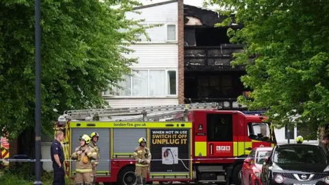 PA Media A fire engine and firefighters outside a burned-out residential building