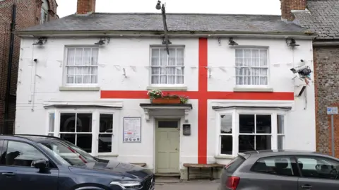 Andrew Matthews/PA Wire A St George's flag has been painted outside of a pub which has a row of cars parked outside of it.