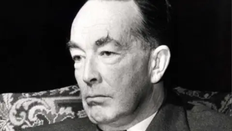 Lord Hartley Shawcross wearing a suit and tie in a black and white photo as he is interviewed by the BBC